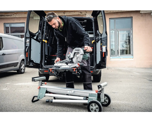 Mann mit Metabo Kapp- und Gehrungssäge auf einem Sägetisch vor einem Transporter