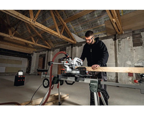 Mann arbeitet mit einer Metabo Kappsäge in einem Rohbau, um ein Holzbrett zu schneiden.