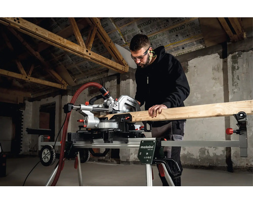 Un homme scie du bois avec une scie à onglet Metabo sur un support de scie à onglet dans un bâtiment en construction.