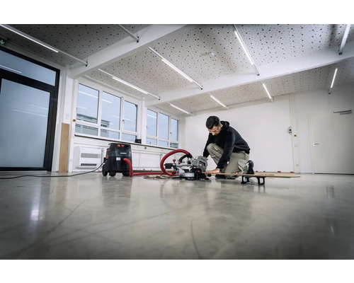 Une personne travaille avec une scie à onglet et un aspirateur dans une pièce lumineuse.