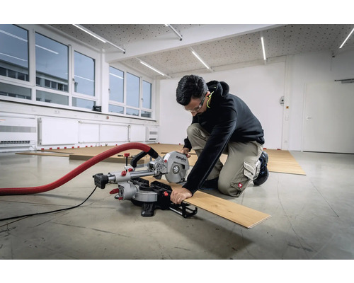 Une personne coupe une planche de bois avec une scie à onglet Metabo dans une pièce avec un plancher en bois.