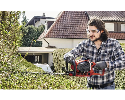 Un homme taille une haie avec un taille-haie dans le jardin.