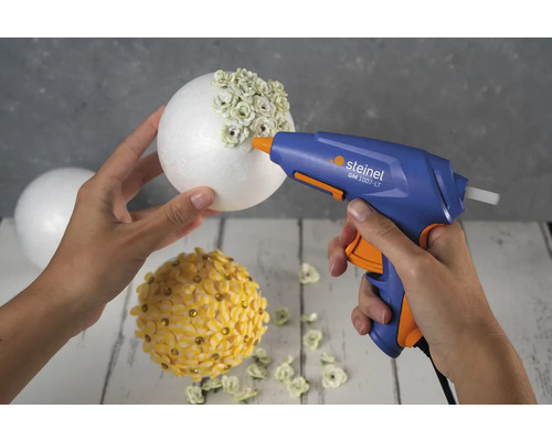Une personne utilise un pistolet à colle chaude pour fixer des décorations sur une boule en polystyrène