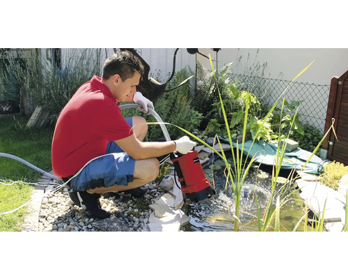 Un homme utilise une pompe de bassin pour vider un bassin de jardin.