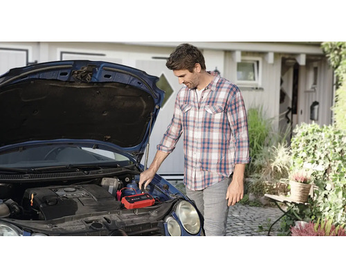 Mann schließt Starthilfe-Gerät an Autobatterie an