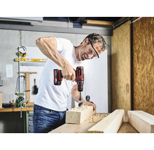 Un homme perce un trou dans une pièce de bois avec une perceuse sans fil.