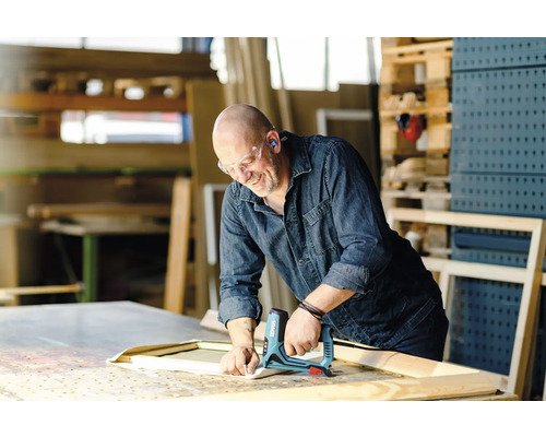 Ein Handwerker befestigt mit einem elektrischen Tacker Stoff an einem Holzrahmen in einer Werkstatt.