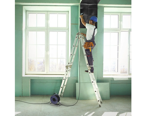 Ein Handwerker befestigt eine Dämmplatte auf einer Baustelle mit einer Leiter.