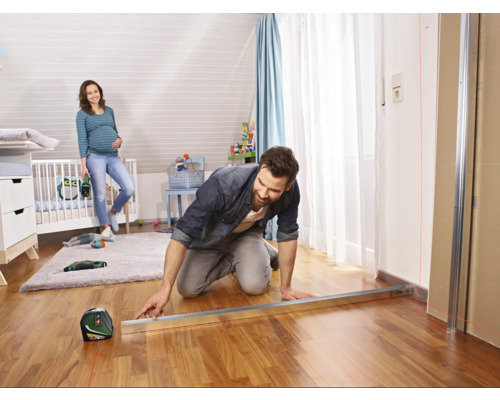 Un homme travaille avec un niveau laser dans une chambre d''enfant, tandis qu''une femme enceinte se tient en arrière-plan.