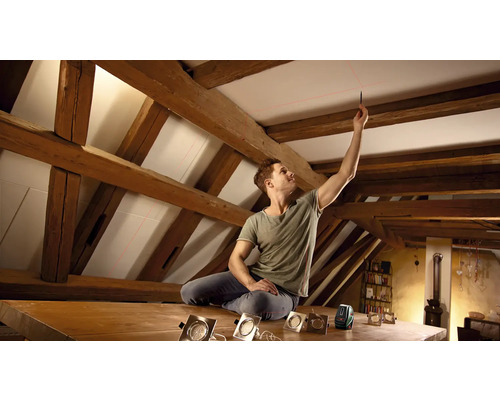 Mann benutzt einen Linienlaser zur Ausrichtung in einem Dachzimmer mit Holzrahmen.