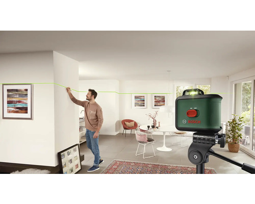 Un homme utilise un laser lignes croisées Bosch dans un salon lumineux.