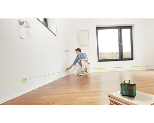Un homme utilise un laser à lignes Bosch pour marquer une ligne verte sur un mur dans une pièce.