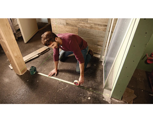 Un homme marque une surface de sol avec un laser à lignes et du ruban adhésif