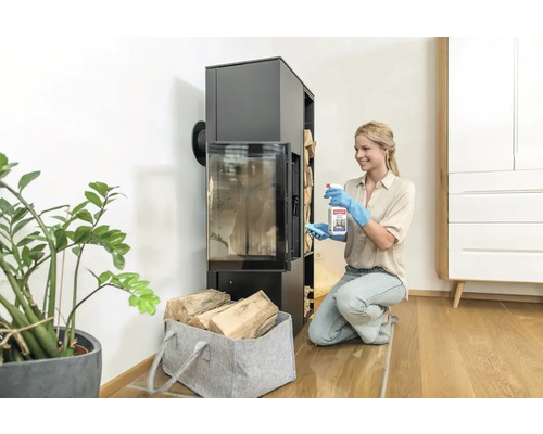 Frau reinigt Kaminofen mit Reinigungsmittel