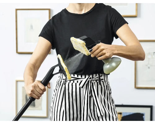 Une personne utilise un nettoyeur vapeur avec différents accessoires pour le nettoyage dans un intérieur.