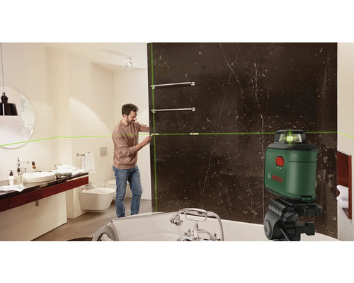 Un homme utilise un laser linéaire dans une salle de bains pour aligner des porte-serviettes.