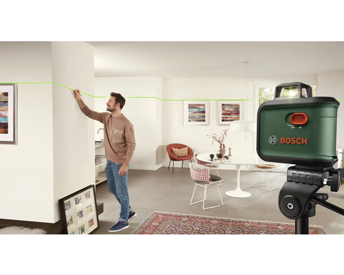 Un homme utilise un laser linéaire de Bosch dans un salon pour marquer une ligne sur un mur. Le laser est placé sur un trépied.