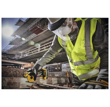 Un artisan portant des lunettes de protection et un gilet de sécurité coupe un morceau de métal avec une meuleuse DeWalt.