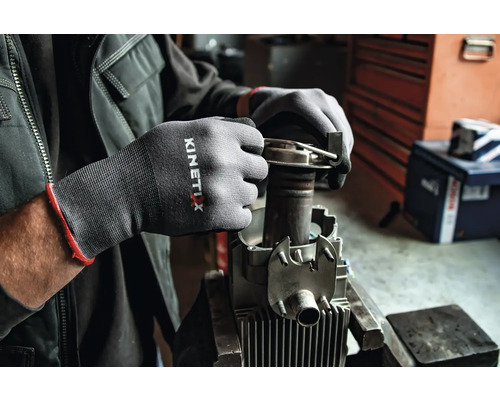 Les mains d''une personne portent des gants de travail Kinetix lors de la réparation d''une machine.