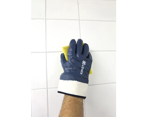 Eine Hand mit KINETIXX Arbeitshandschuh wischt mit einem Schwamm eine geflieste Wand.