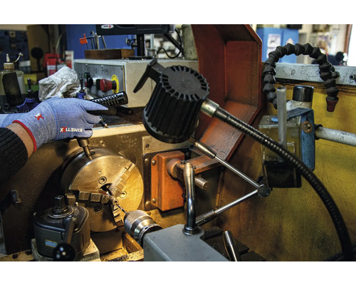 Eine Person mit Arbeitshandschuhen bedient eine Drehmaschine.