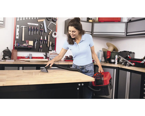 Eine Frau reinigt eine Werkbank mit einem Nass Trockensauger in einer Werkstatt.