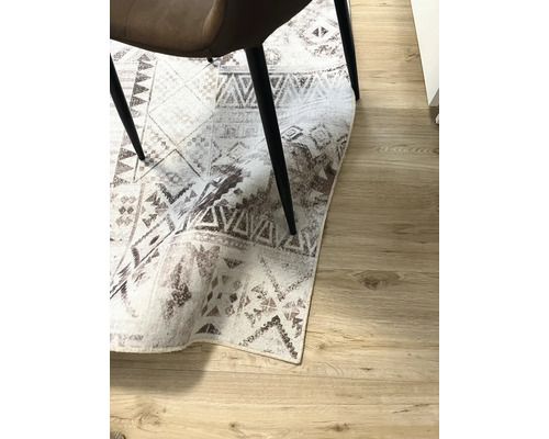 Tapis décoratif avec motifs géométriques sous une chaise sur un plancher en bois.