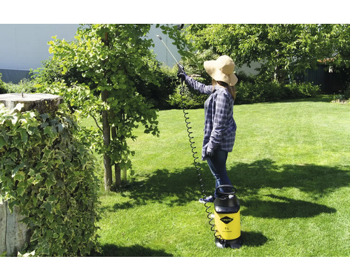 Frau verwendet eine gelbe Druckspritze von Mesto im Garten, um einen Baum zu behandeln.