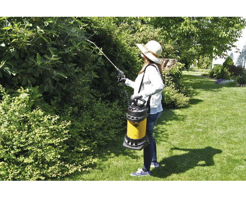 Frau sprüht Sträucher mit einer Gartenspritze im Garten.