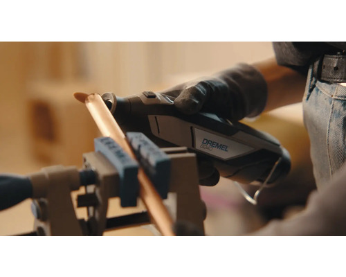 Une personne utilise un outil multifonction Dremel 8240 pour couper un tuyau de cuivre fixé dans un étau.