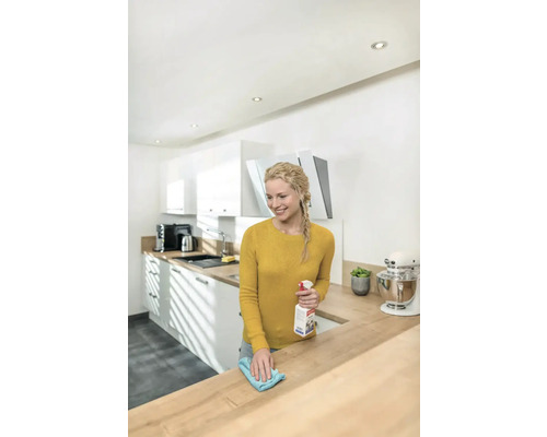 Frau reinigt mit einem Reinigungsmittel und einem Tuch eine Küchenarbeitsplatte.