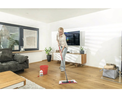 Femme nettoie le parquet avec un nettoyant et une serpillière dans le salon