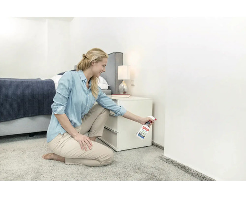 Frau sprüht Reinigungsmittel in einer Schlafzimmerecke