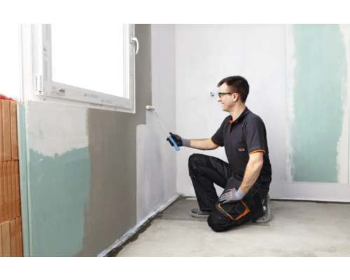 Un homme peint un mur avec un rouleau à peinture dans une pièce.