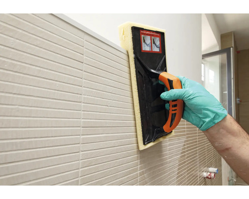 Fliesenleger reinigt eine Wand mit einem Fugenschwammbrett.