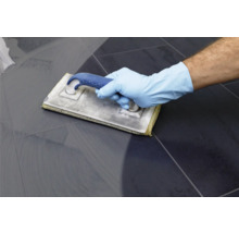 Une main gantée utilise une planche à laver pour nettoyer les carreaux.