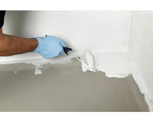 Une personne scelle un coin de mur de plancher avec un rouleau de peinture et un revêtement imperméable.