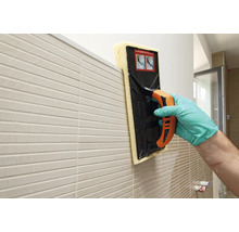 Carreleur nettoyant un mur carrelé avec une éponge.