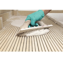 Main avec gant et spatule lors de la pose de carreaux