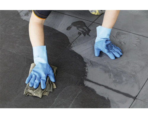 Une personne nettoie des carreaux avec un chiffon et des gants.
