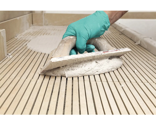 Carreleur appliquant de la colle avec une spatule sur le sol.