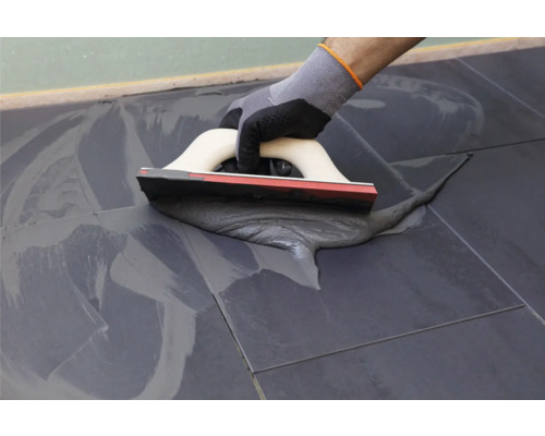 Carreleur utilisant une raclette à joints pour jointoyer des carreaux