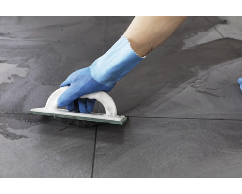 Une personne joint des carreaux avec une taloche à joints.