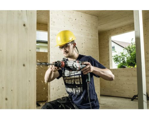 Un homme perce un trou dans un mur en bois avec une perceuse