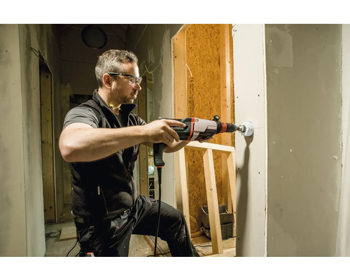 Un homme perce un trou dans une cloison sèche avec une perceuse Metabo.