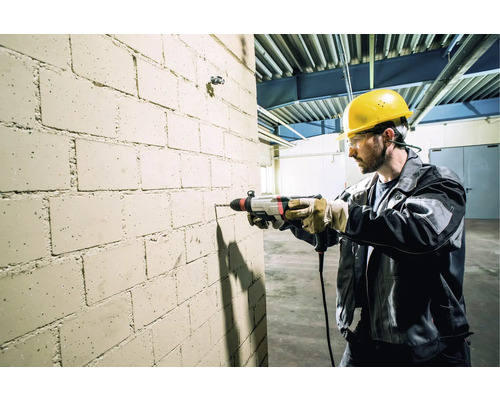 Un artisan perce un trou dans un mur de briques avec une perceuse.