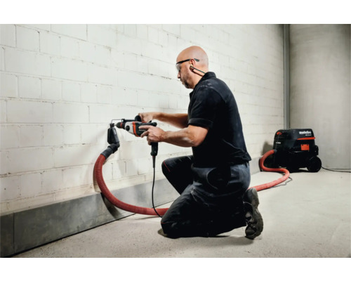 Un artisan perce un trou dans un mur avec un perforateur, aspiration des poussières raccordée