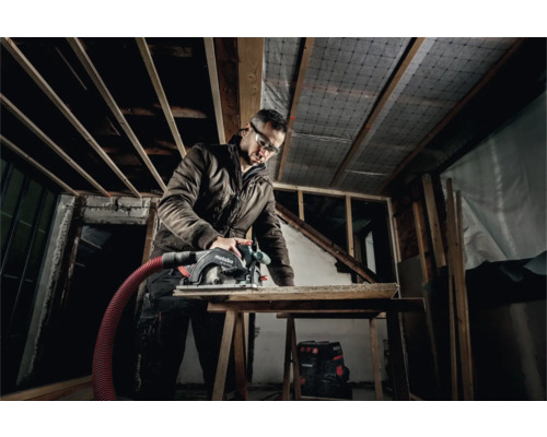 Handwerker mit Schutzbrille sägt Holz mit einer Handkreissäge von Metabo in einem Rohbau.