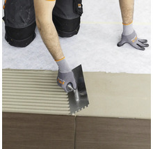Carreleur appliquant de la colle sur des carreaux avec une spatule crantée.