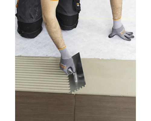 Fliesenleger trägt Kleber mit einer Zahnspachtel auf Fliesen auf.